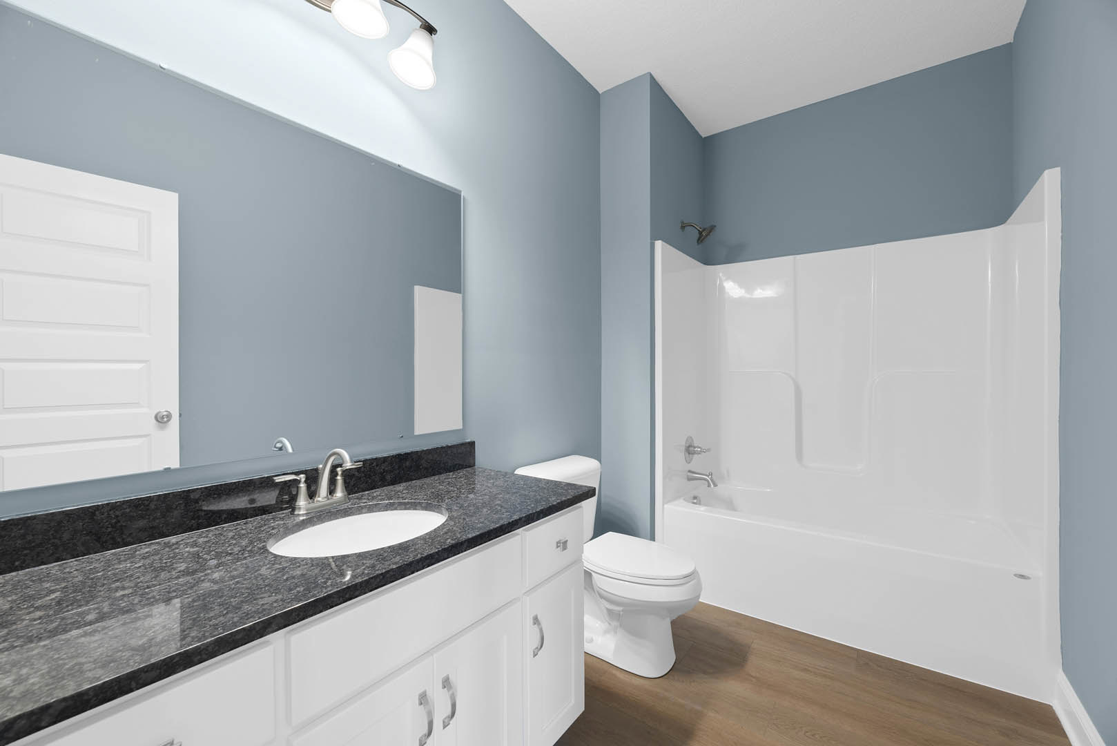 Modern bathroom with white tile walls, built-in shower, white porcelain sink set in a wood vanity, matching toilet, and chrome fixtures