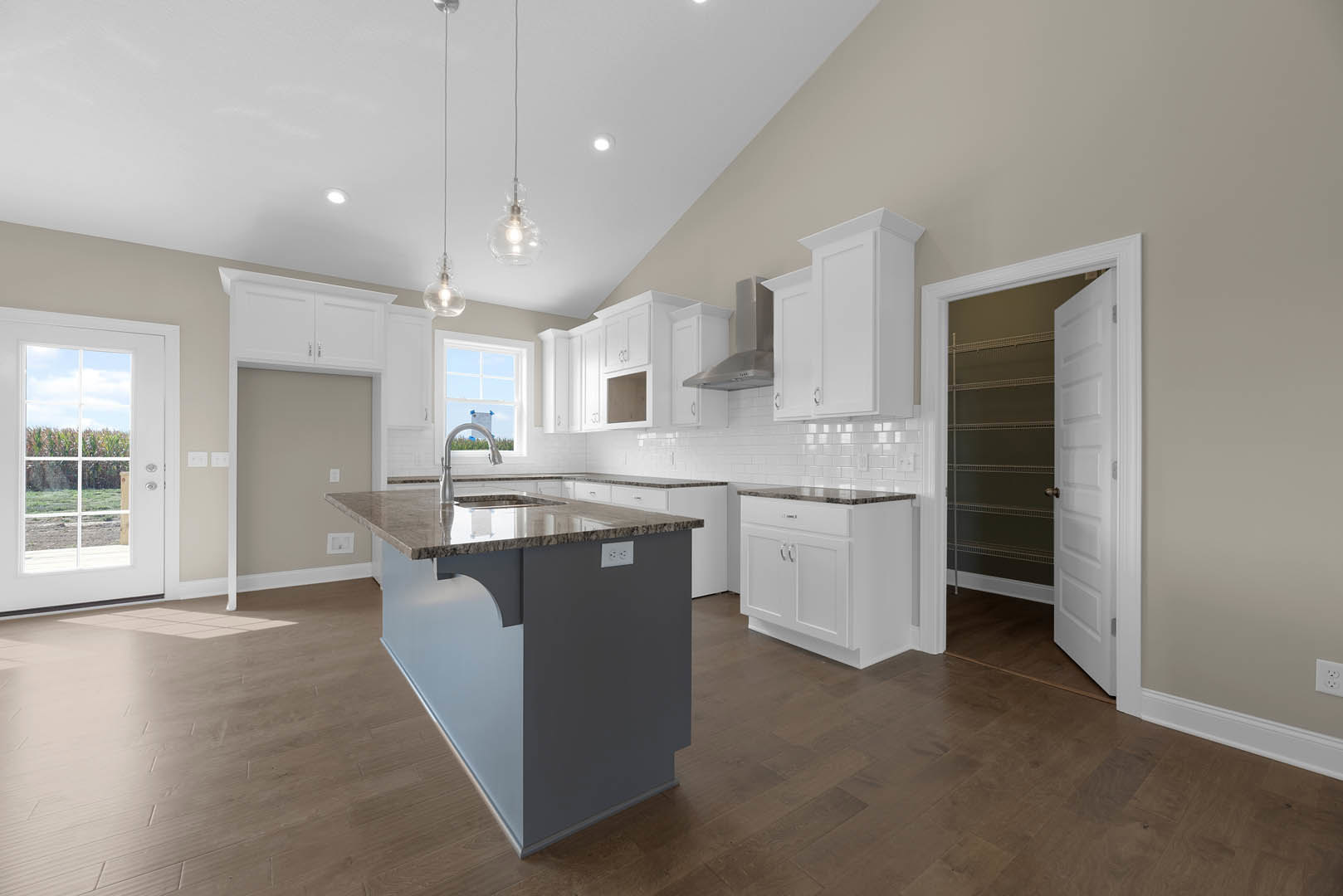 Spacious kitchen featuring a large marble-topped island, white cabinetry, glass-paneled door, stainless steel faucet, and pendant light fixtures