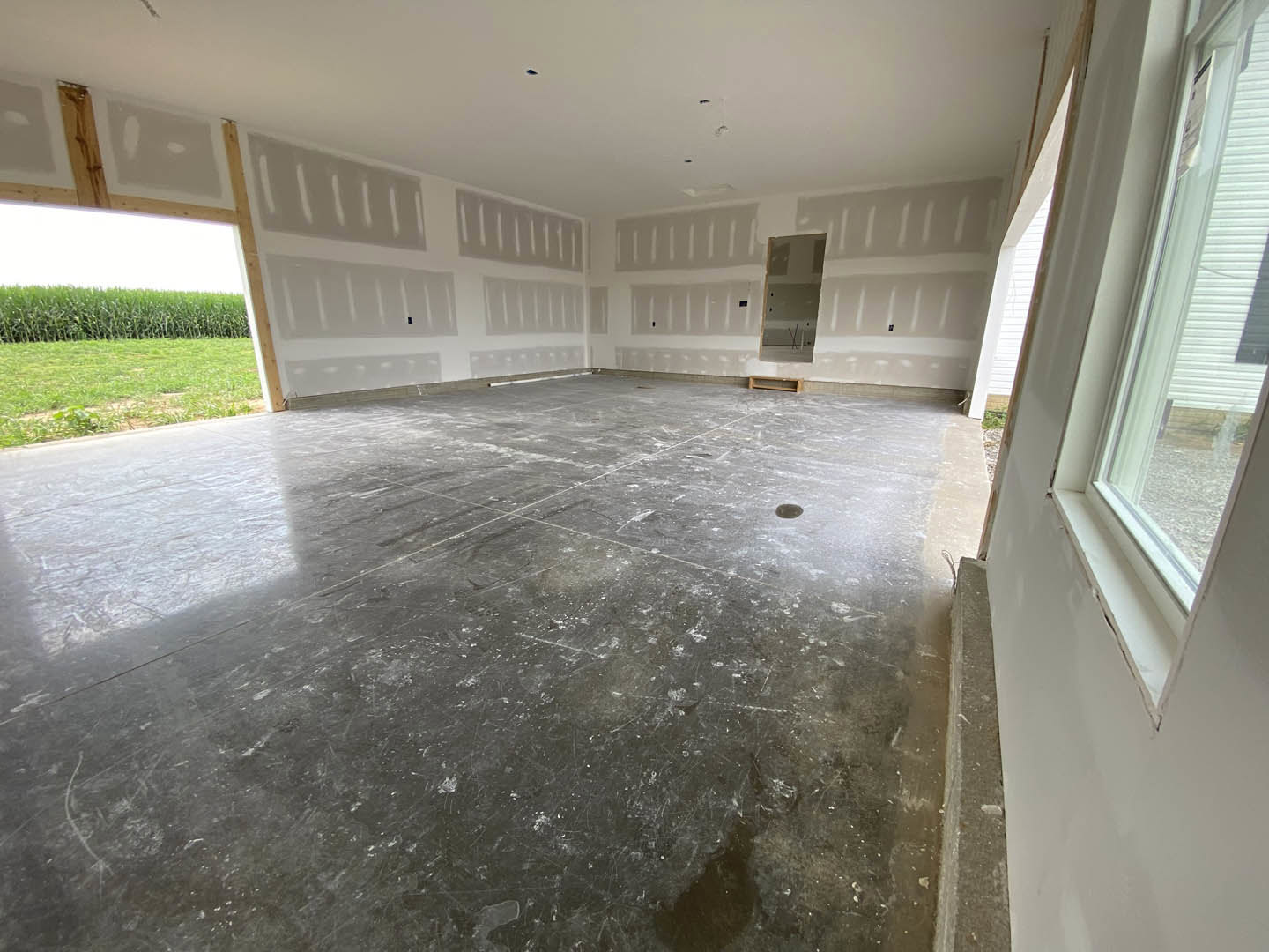 Modern interior room featuring a large window overlooking a field of green grass, grey flooring with subtle white lines, plaster walls, and a ceiling with recessed lighting.
