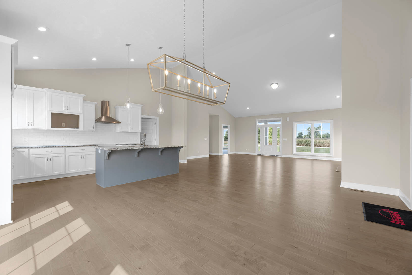 Spacious open floor plan featuring hardwood floors, white marble kitchen island, glass-framed light fixture, cabinetry, and large window overlooking a field