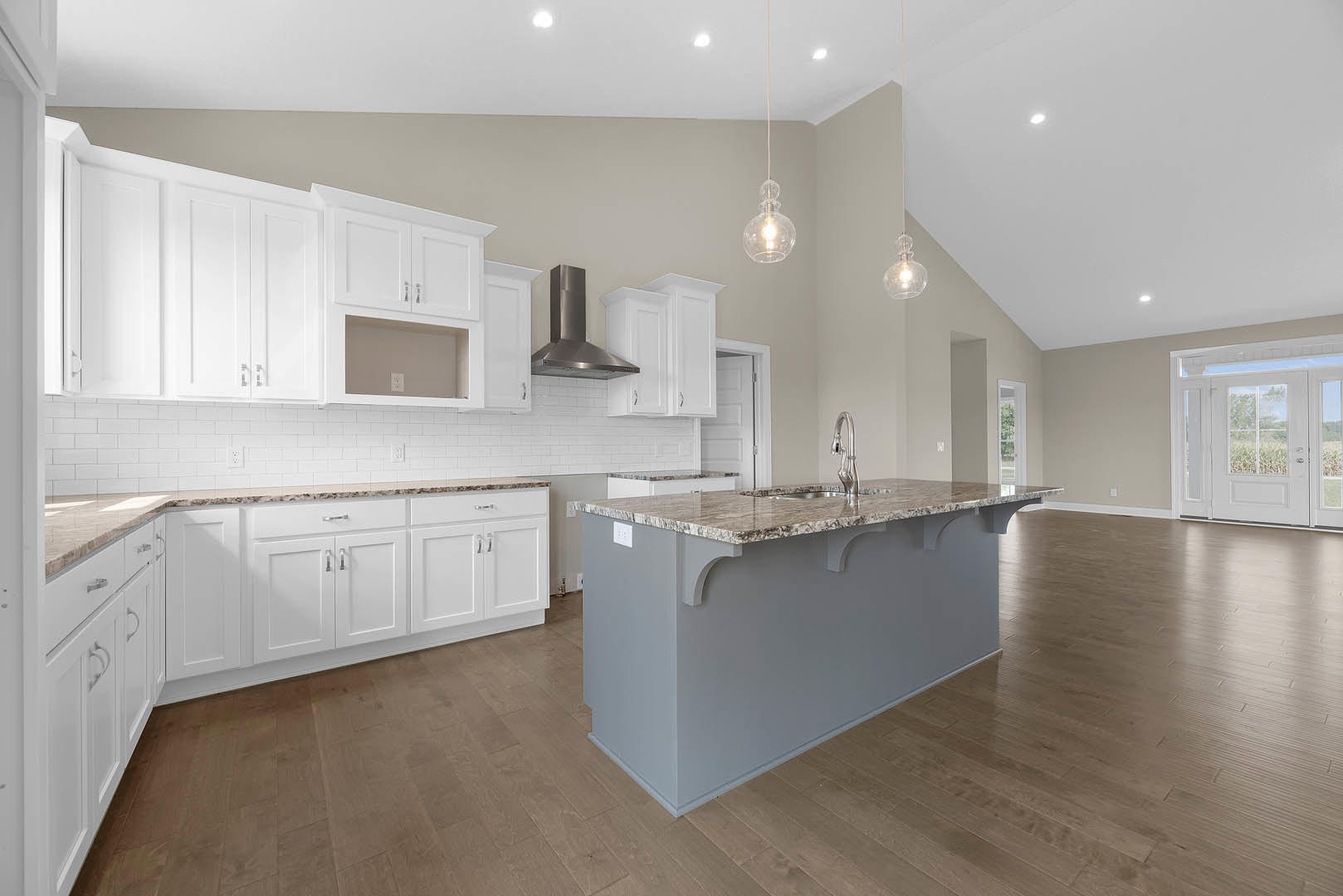 Spacious kitchen featuring a large marble-topped island with built-in sink, stainless steel exhaust hood above stove, white cabinetry, tile flooring, glass-paneled door, and modern