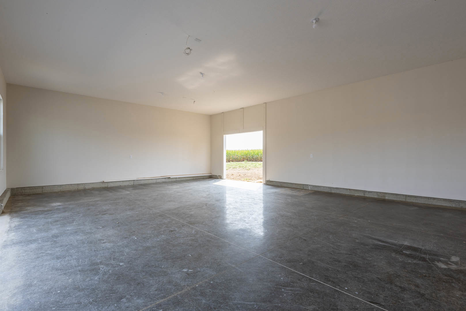 Grey tile floor in a room with a large window overlooking a cornfield, white plaster ceiling with a visible hole, natural light streaming through doorway, close-up of exposed wire