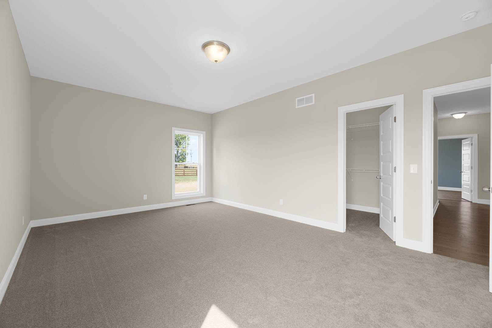 Carpeted room with a white-framed window overlooking grass and a fence, open door leading to wood laminate flooring, ceiling-mounted light fixture, plaster walls