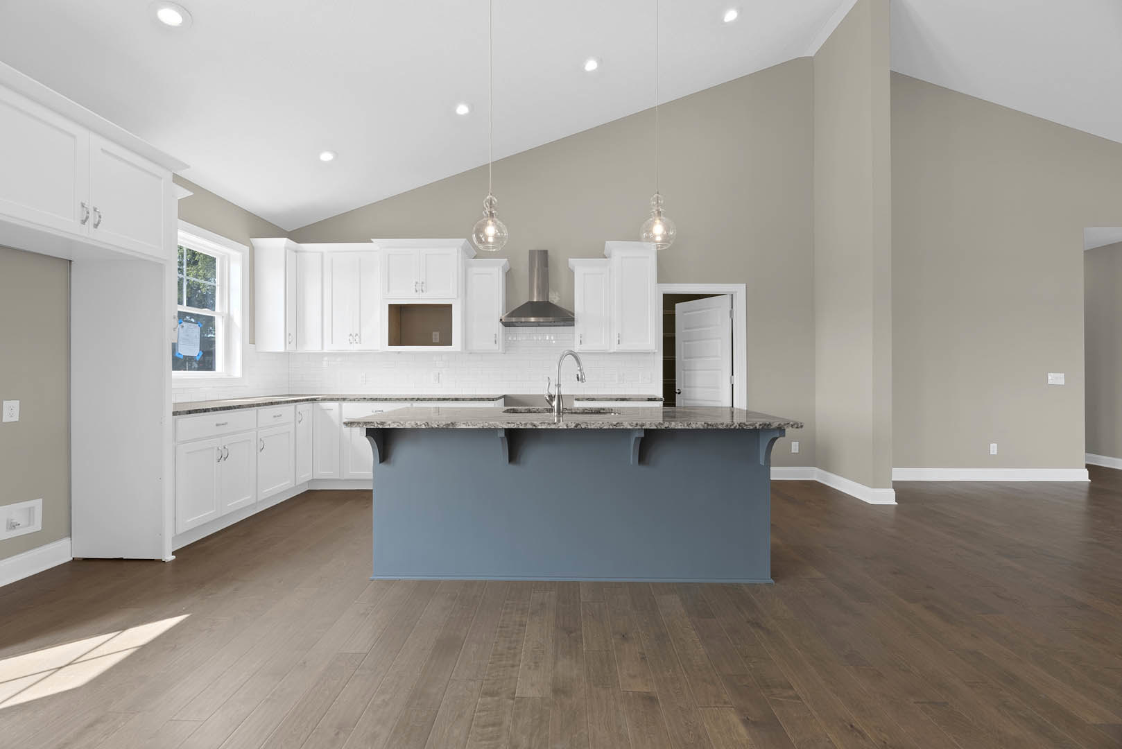 White shaker cabinets and matching island with quartz countertop, stainless steel sink, wood laminate flooring, blue accent wall, recessed ceiling lights, and vent detail