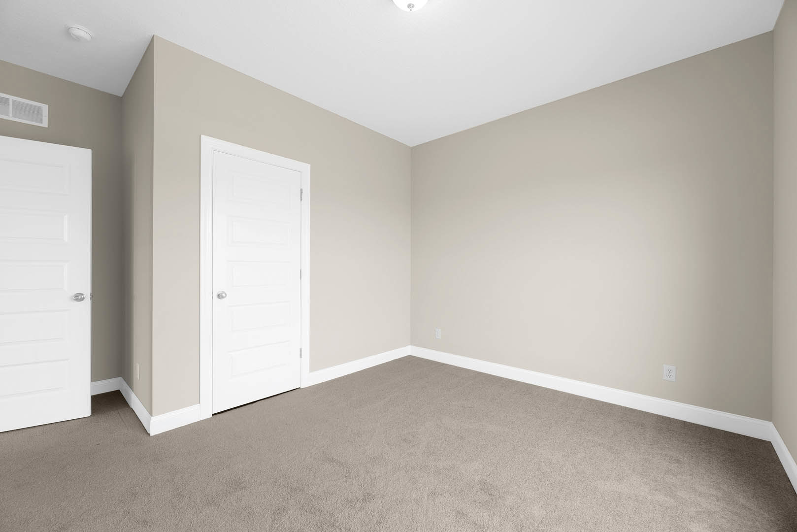 White paneled door with silver handle, beige carpet flooring, white walls, ceiling vent, recessed lighting, man standing beneath light fixture
