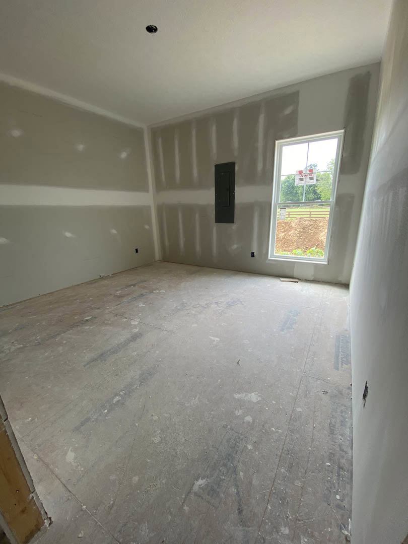 Bright room with white plaster walls, large window overlooking a dirt hill, black and white doors, wood flooring, and a sign with red squares on the window.