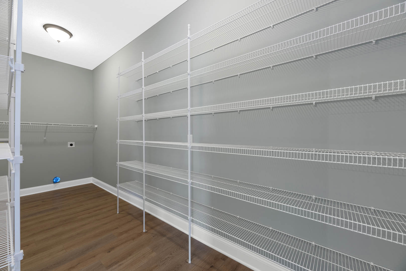 Room with white wire shelving along plaster walls, wood flooring, ceiling light fixture, and a window; shelves display a small sign.
