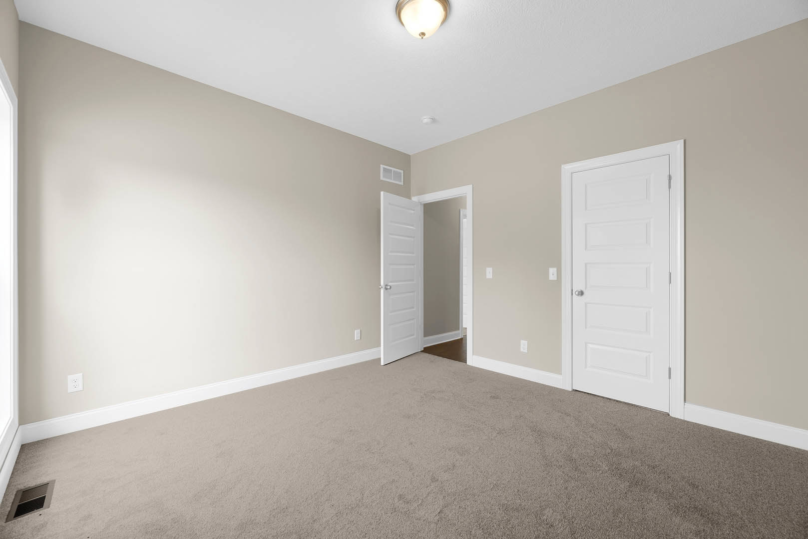 Carpeted room with white paneled doors, silver door knob, white walls, wall vent, and ceiling light fixture
