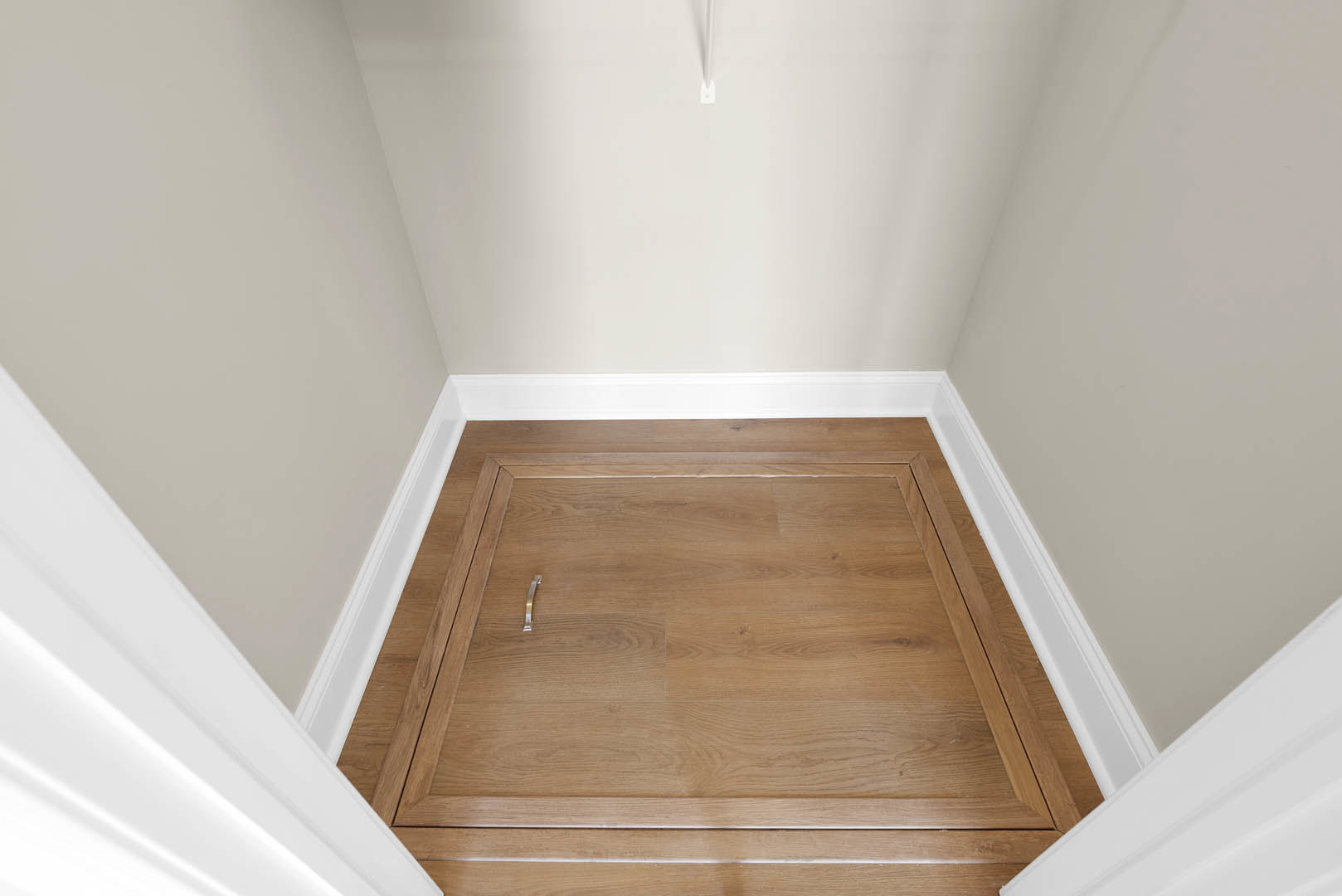 Light hardwood floor with natural varnish, white plaster walls, simple base molding, open doorway, and minimal interior decor