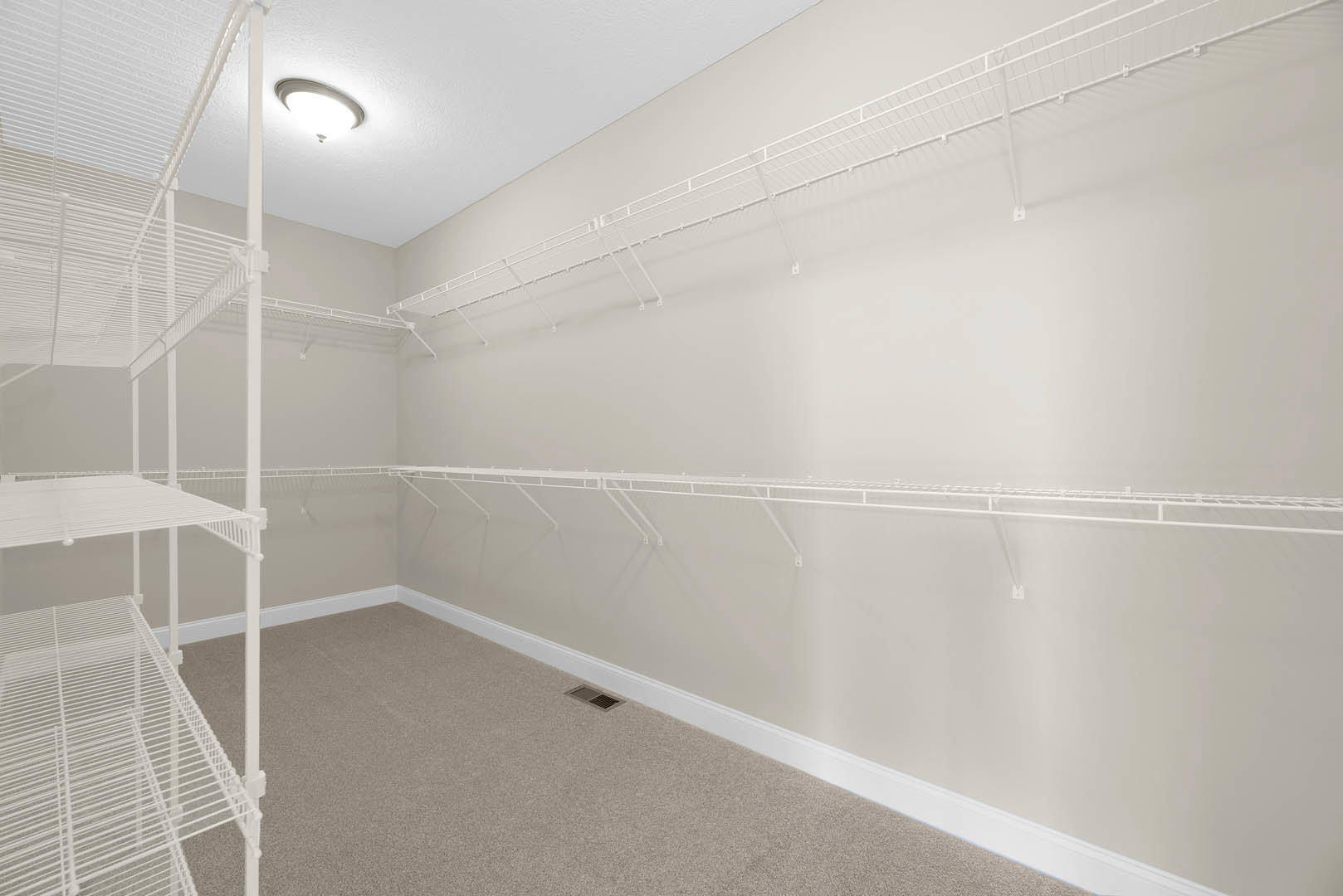 Empty walk-in closet with white wire shelving, light fixture on ceiling, and vent above plaster walls.