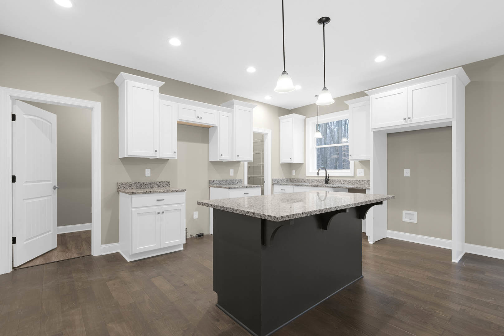 Kitchen with white shaker cabinets, black and white island featuring granite countertop, stainless steel sink, silver hardware, tiled floor, recessed ceiling lights, and white door