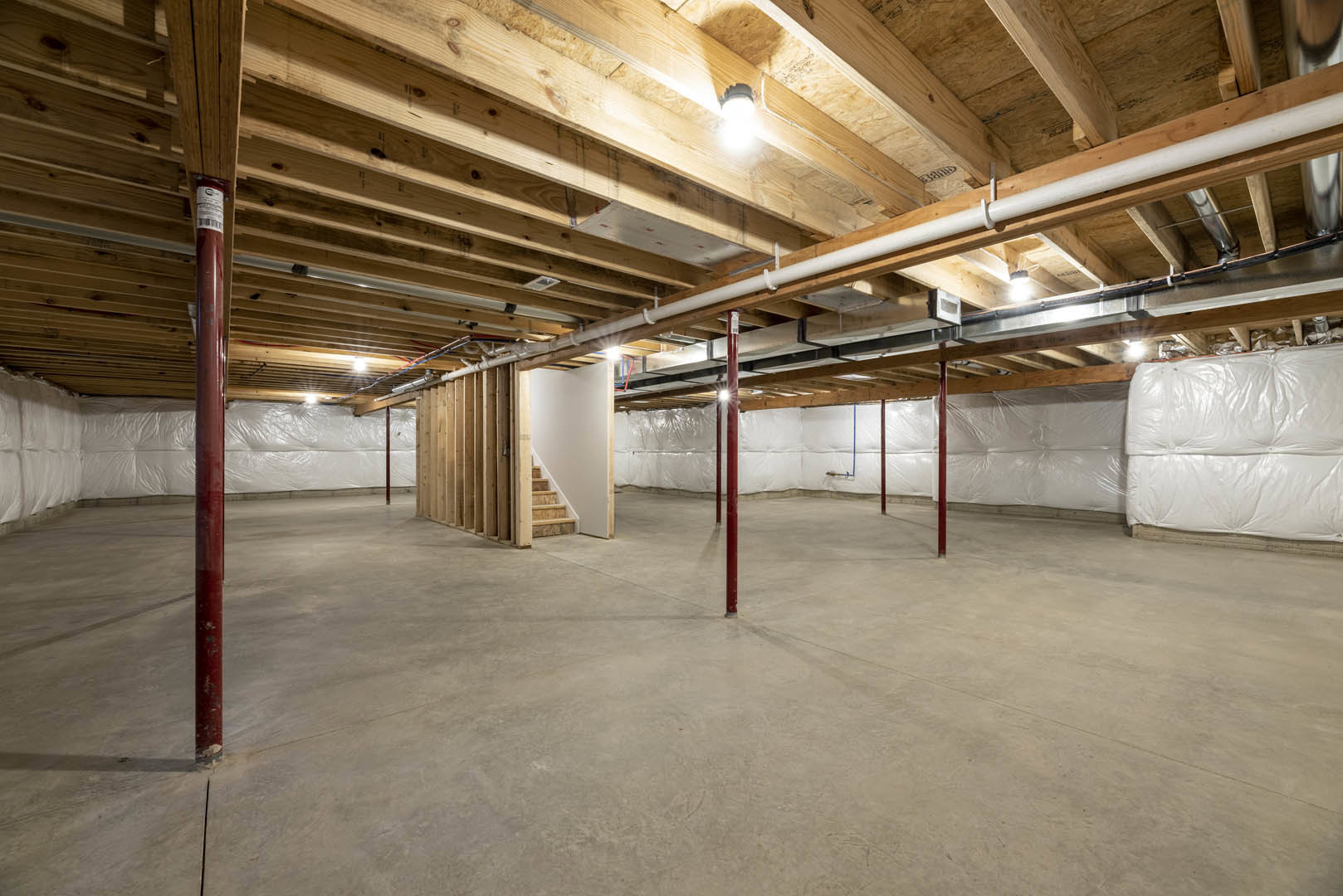 Exposed wooden ceiling beams above a spacious room with a staircase, light fixture, and wood flooring