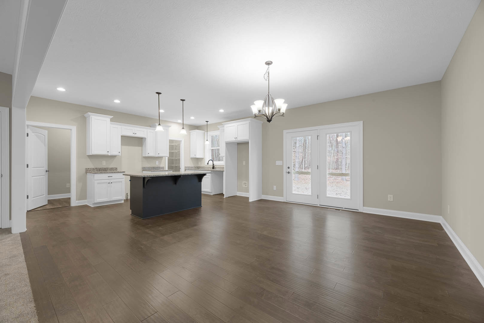 Spacious kitchen with wood flooring, black and white countertops on a central island, glass-paneled double doors, and a ceiling-mounted chandelier.