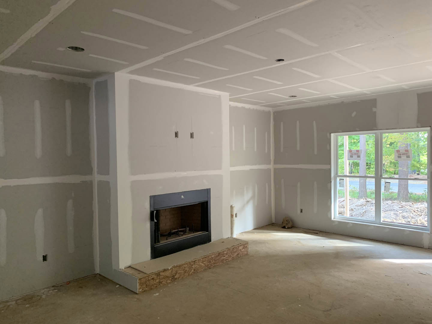 Modern den with plaster walls, concrete floor, glass-door fireplace, large window displaying signs, and visible step in foreground