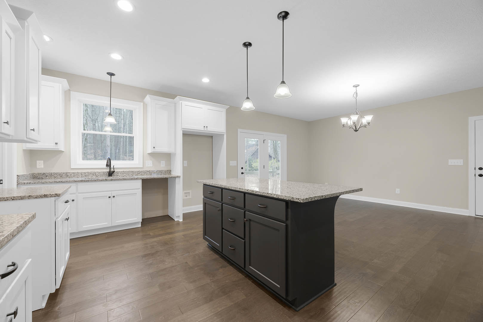 Kitchen with wood flooring, central island featuring marble countertop and drawers, stainless steel sink, modern light fixture mounted on black pole, white walls, and built-in