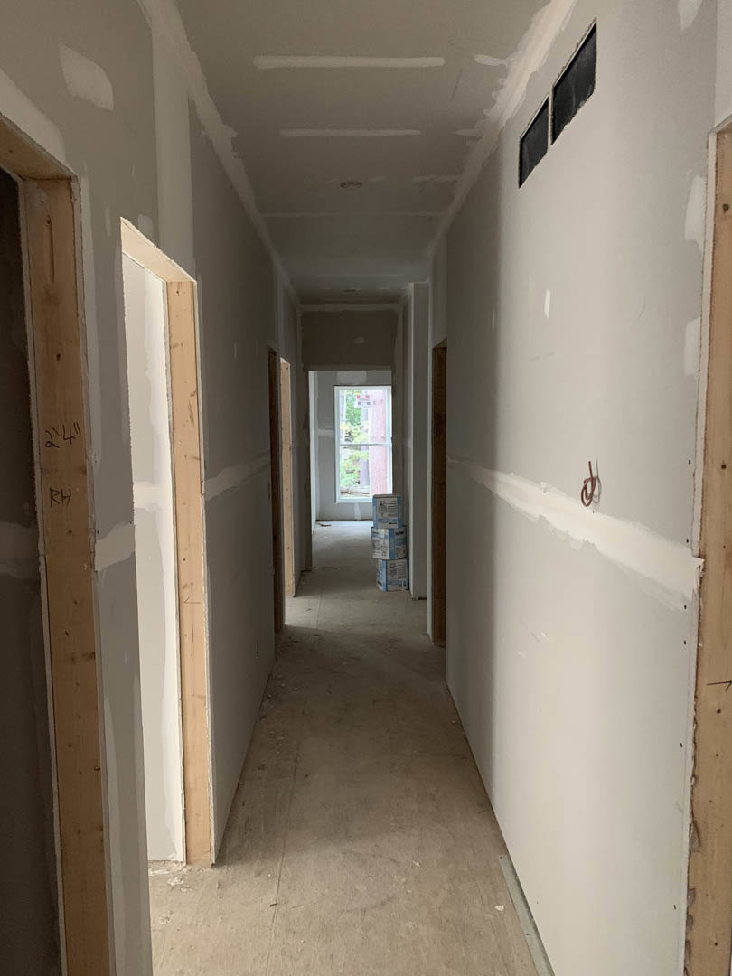 Hallway with smooth white plaster walls, rectangular window with white frame, light wood flooring, scattered cardboard boxes, red pipe along wall, white ceiling