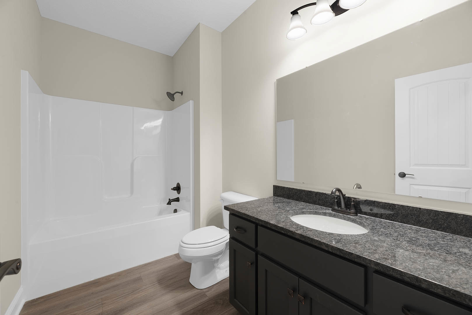 Bathroom with white freestanding bathtub, white vanity cabinet with black hardware, white sink, and modern black faucet, set against light tile walls and flooring.