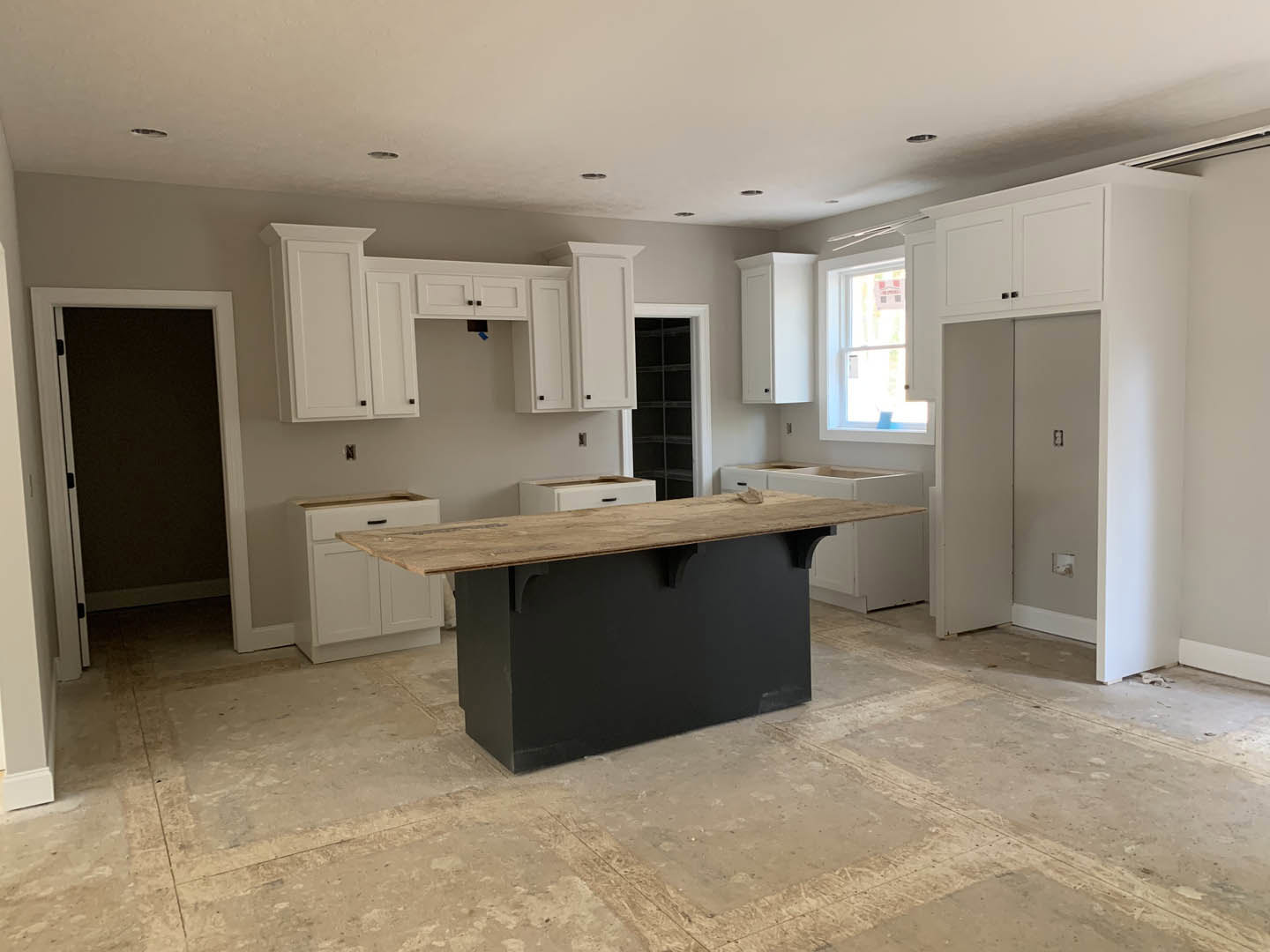 White kitchen cabinets, wood-topped black island, tile flooring, dining table, black screen door with white frame, white door with sign, white rectangular appliance with black