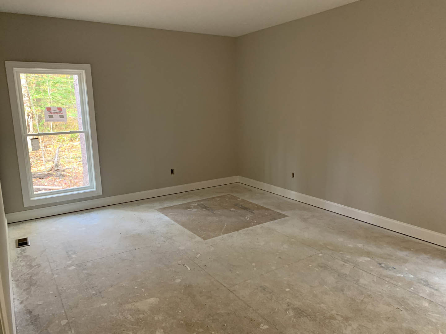Sunlit room featuring a large window, smooth plaster walls, and light-colored tile flooring with a decorative square accent.