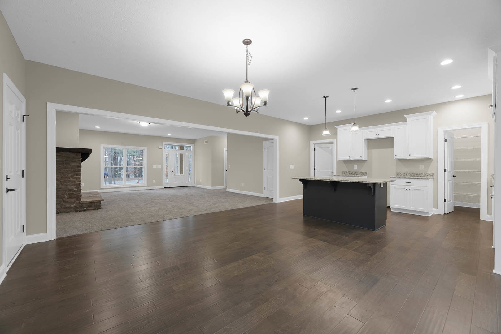 Spacious open floor plan featuring a kitchen island with white countertop, black accent wall, hardwood flooring, modern chandelier, large window overlooking trees, and white door
