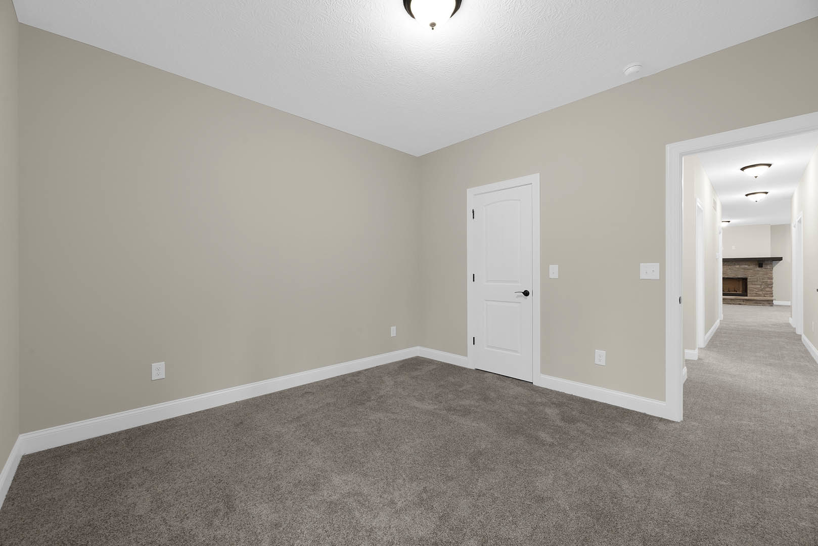 Carpeted room with two white doors featuring black handles, square window with white trim, ceiling light fixture, and light-colored walls with molding