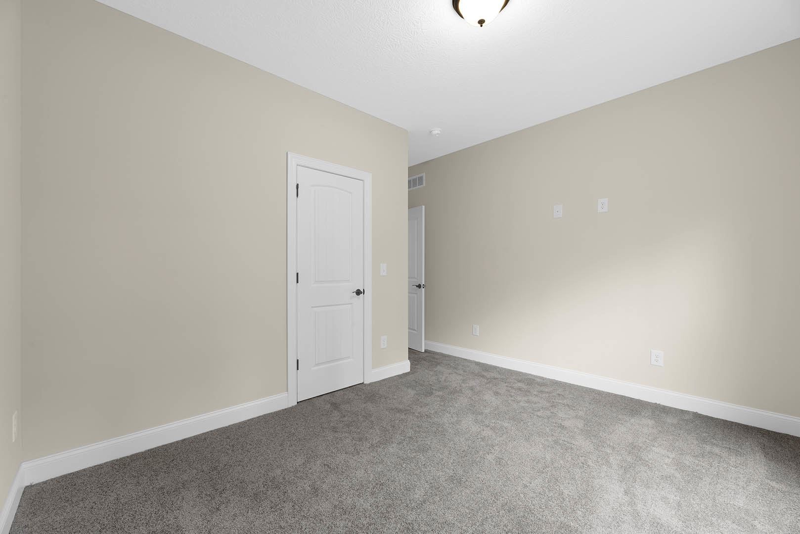 White paneled door with black handles, beige carpeted floor, white walls, recessed ceiling light