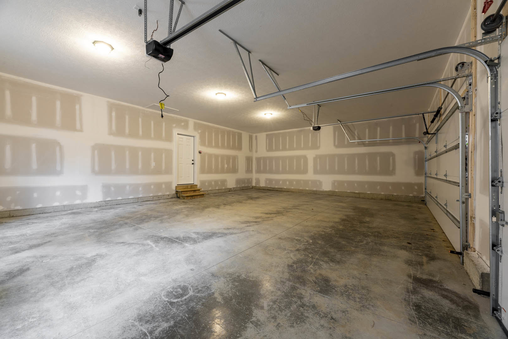 Concrete floor with a few steps, white plaster walls, white door with black knobs, black box mounted on wall, wheel attached to metal pole, empty interior room