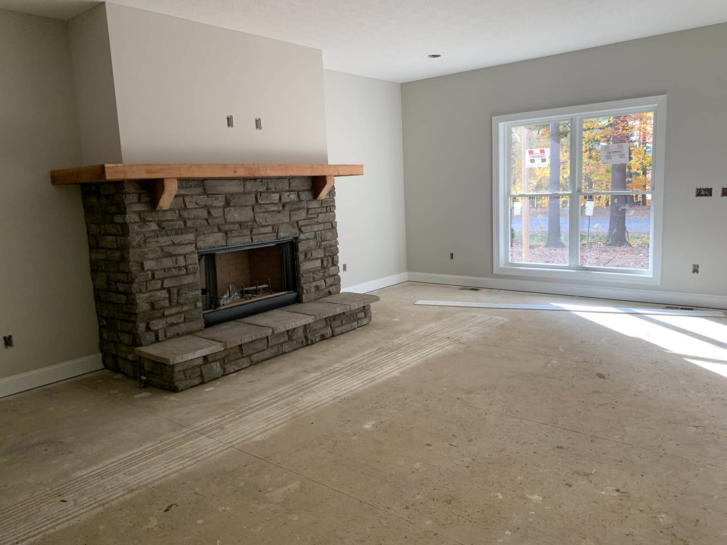 Stone fireplace with wood mantel, brick hearth, and wood sled in a living room; window with sign and stone steps leading to a door visible.