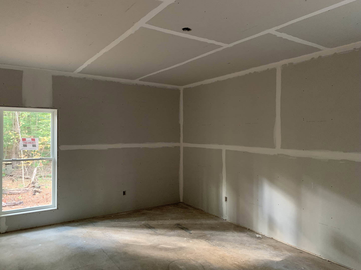 White plaster walls, large window with a sign, smooth concrete floor, black mark on ceiling, natural daylight filling the room