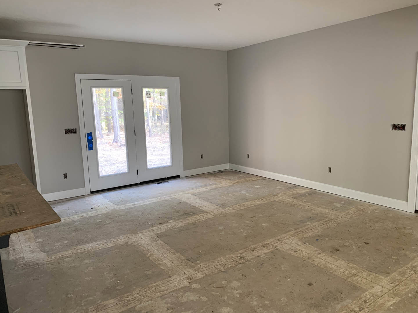 White double doors with glass panels set in a white wall, black handles, wood flooring, and a white ceiling with a round light fixture.