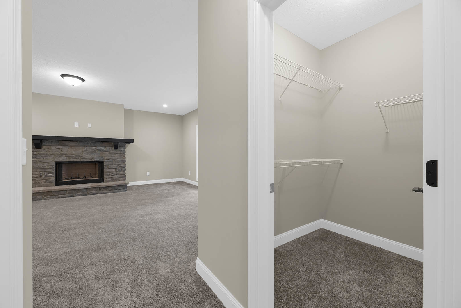 Carpeted room featuring a black-framed fireplace, white shelving, clothes racks, and recessed lighting on plaster walls.