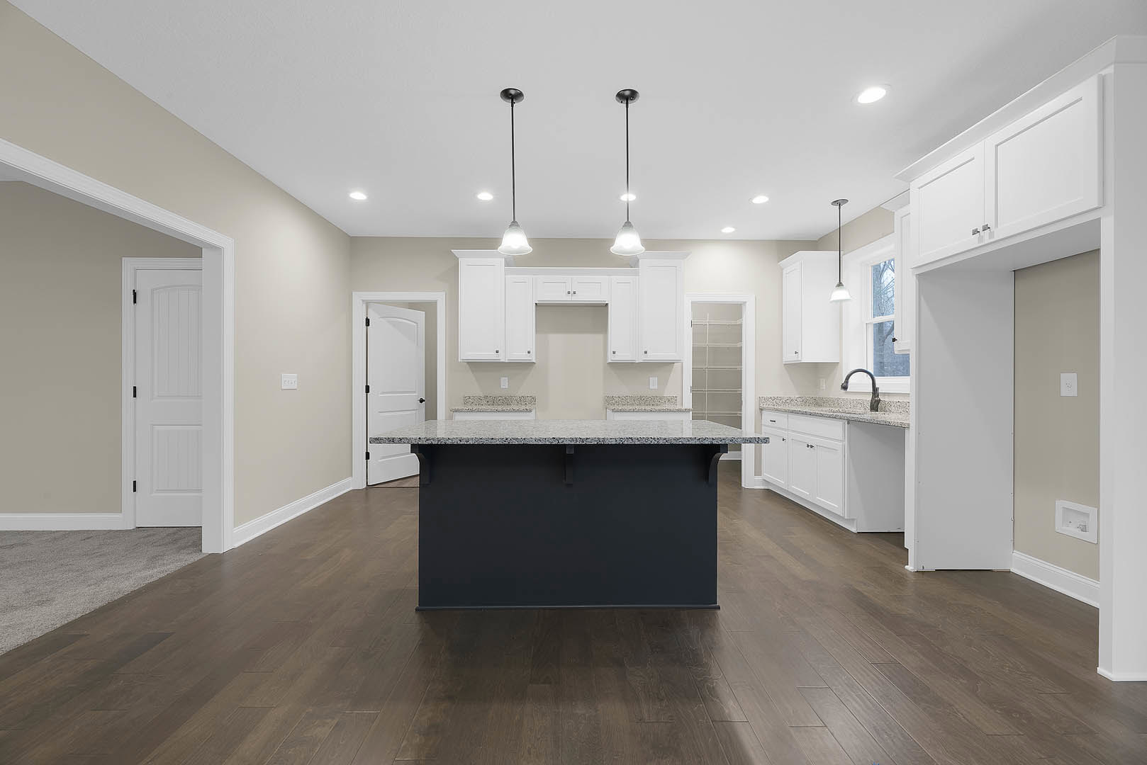 Spacious kitchen featuring a large black-surfaced island, wood flooring, white cabinetry, tile backsplash, stainless steel sink, and modern pendant light fixtures.
