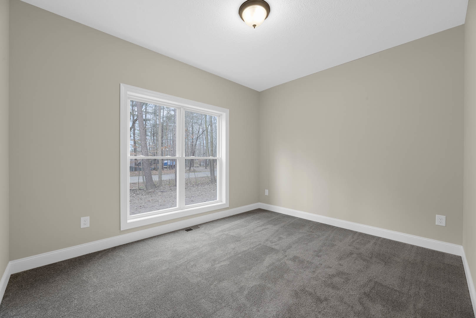 Bright room with large window overlooking trees, grey carpet flooring, white walls with crown molding, and modern ceiling light fixture