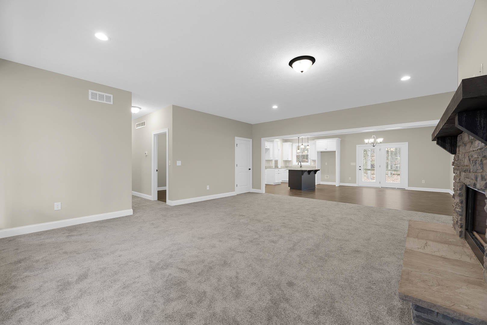 Spacious open-plan room featuring laminate flooring, a modern kitchen with white cabinetry, dining area, double glass-paneled doors, ceiling light fixture, and adjacent carpeted