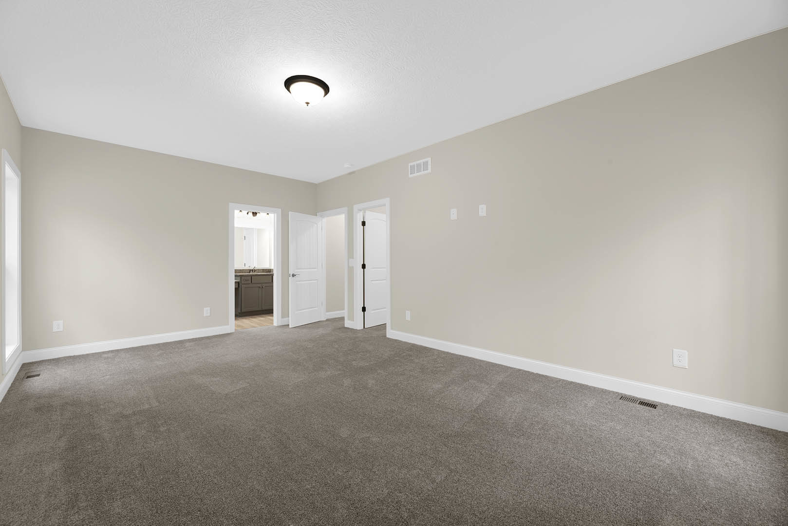 Carpeted room with white walls, white door with silver handle, ceiling light fixture, rectangular window with white frame, partial view into bathroom with sink and mirror