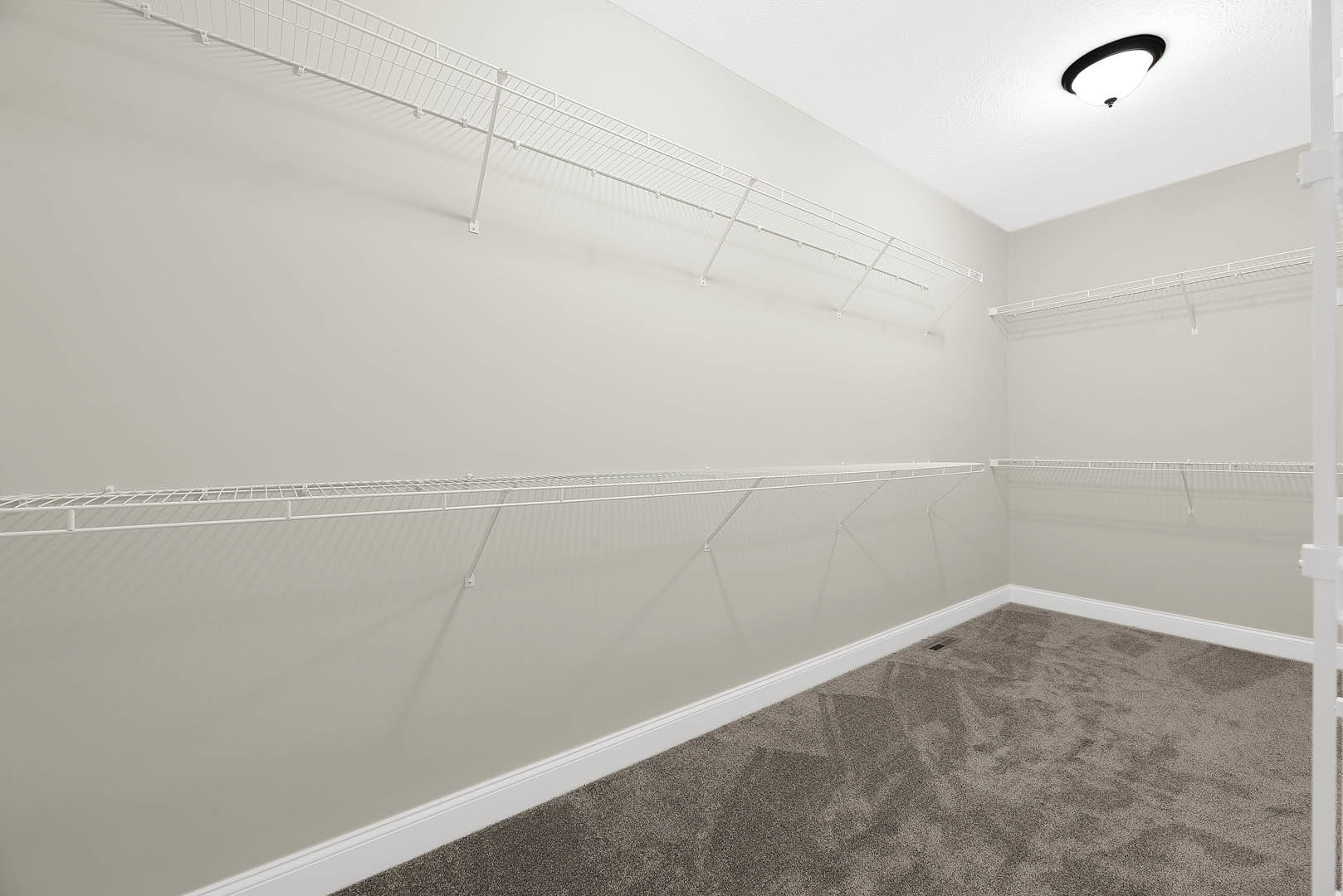 Carpeted room with white built-in shelves, white baseboard, and a white metal closet rod against smooth plaster walls.