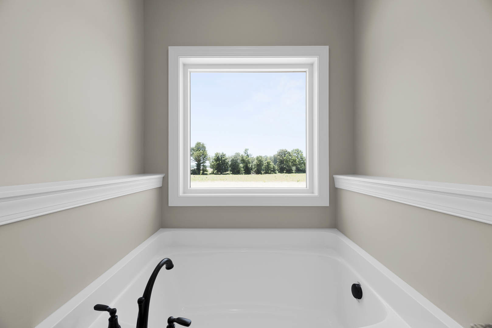 Freestanding white bathtub beneath large window with forest view, chrome faucet, and white shelf on wall