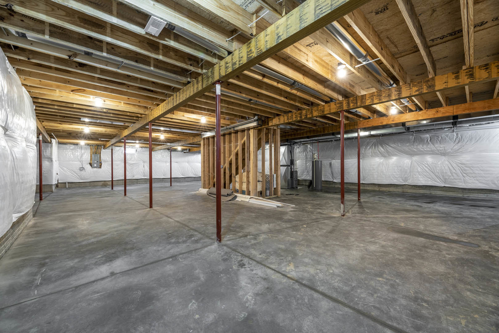 Exposed wood ceiling beams above a concrete floor, red steel support pole, white vent on table, plastic wall covering, unfinished basement interior
