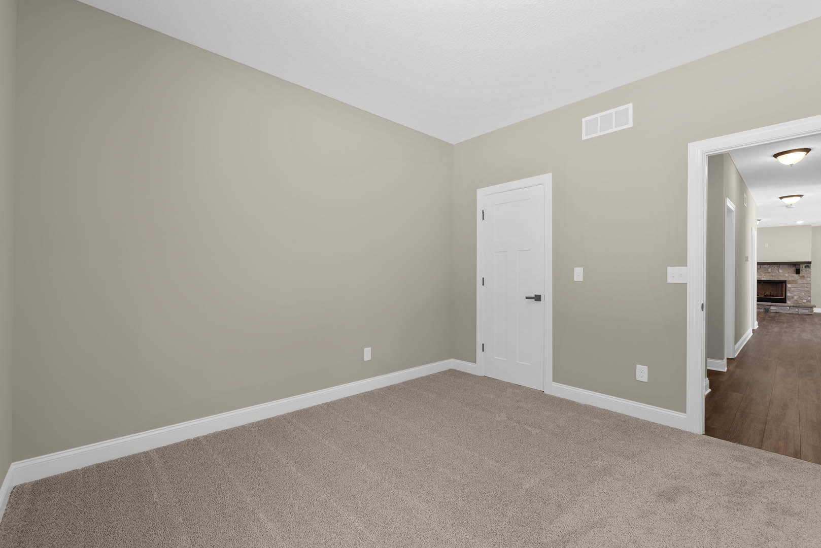 Carpeted room with white trim, white door featuring black handle, white window with matching trim, black-framed fireplace, and hardwood flooring adjacent to carpeted area