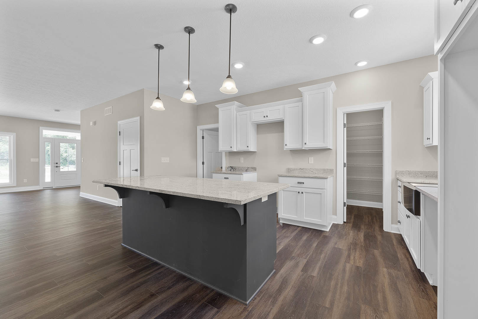 Spacious kitchen featuring a central island with marble countertops, white cabinetry with open shelves, glass-paneled door, laminate flooring, and pendant lighting suspended from a