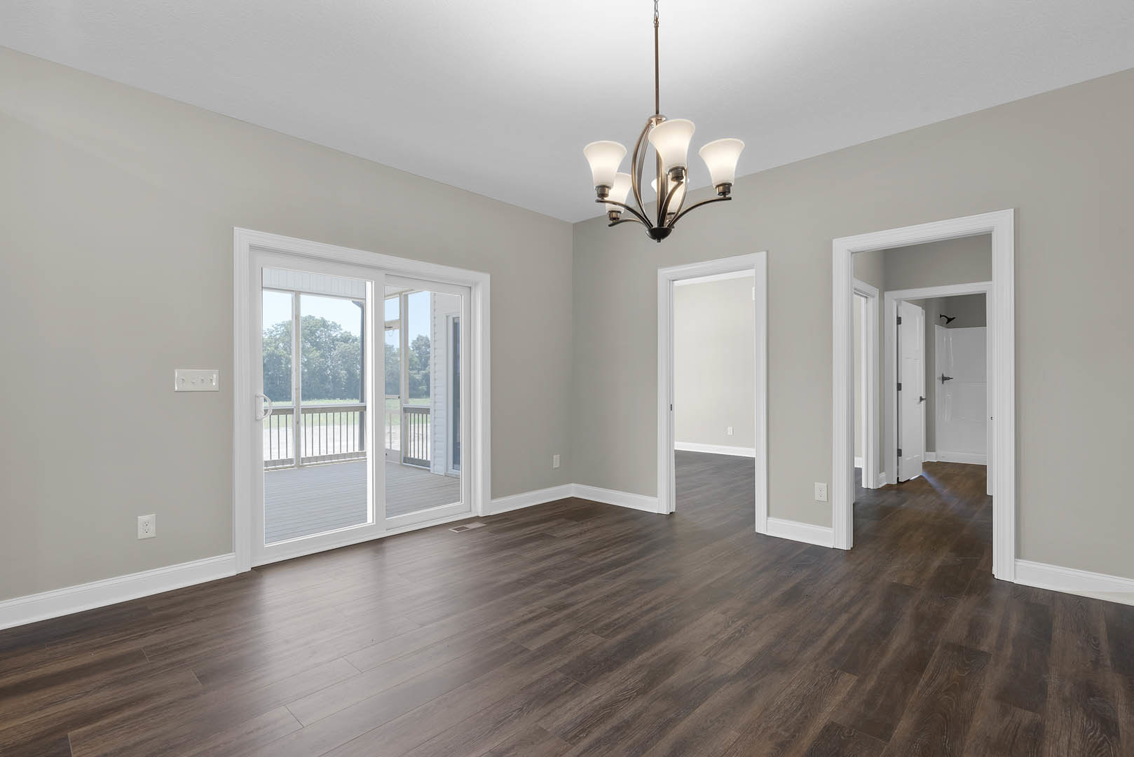 Chandelier hanging from ceiling above hardwood floor, sliding glass door opening to deck, white framed door on adjacent wall, plaster walls with wood trim