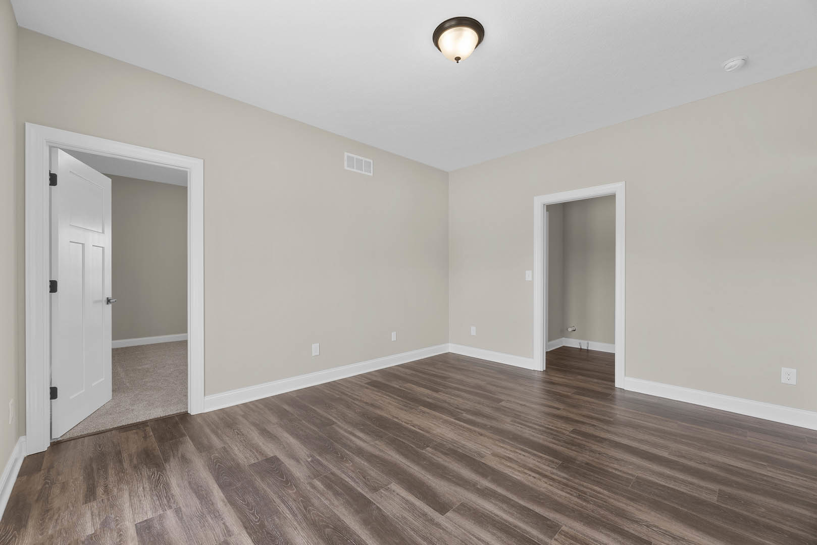 Wood flooring with white baseboards, white walls, a white door with black handle, and a modern light fixture mounted on the ceiling