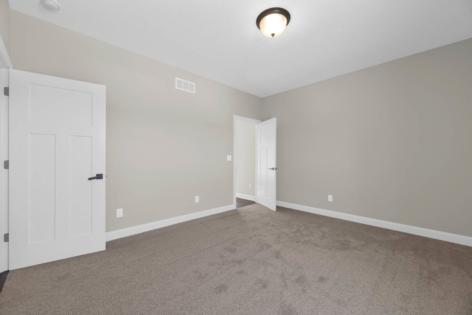 White carpeted room featuring multiple white doors with black and silver handles, ceiling light fixture, white wall vent, and simple molding.