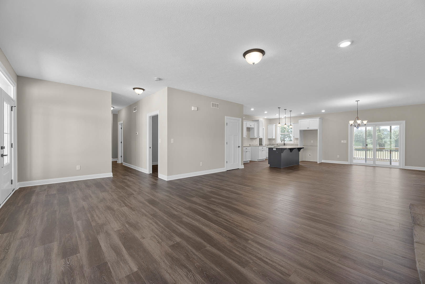 Open-concept kitchen and dining area with hardwood flooring, marble-topped gray island, modern ceiling light fixture, sliding glass door, and white cabinetry with black handles