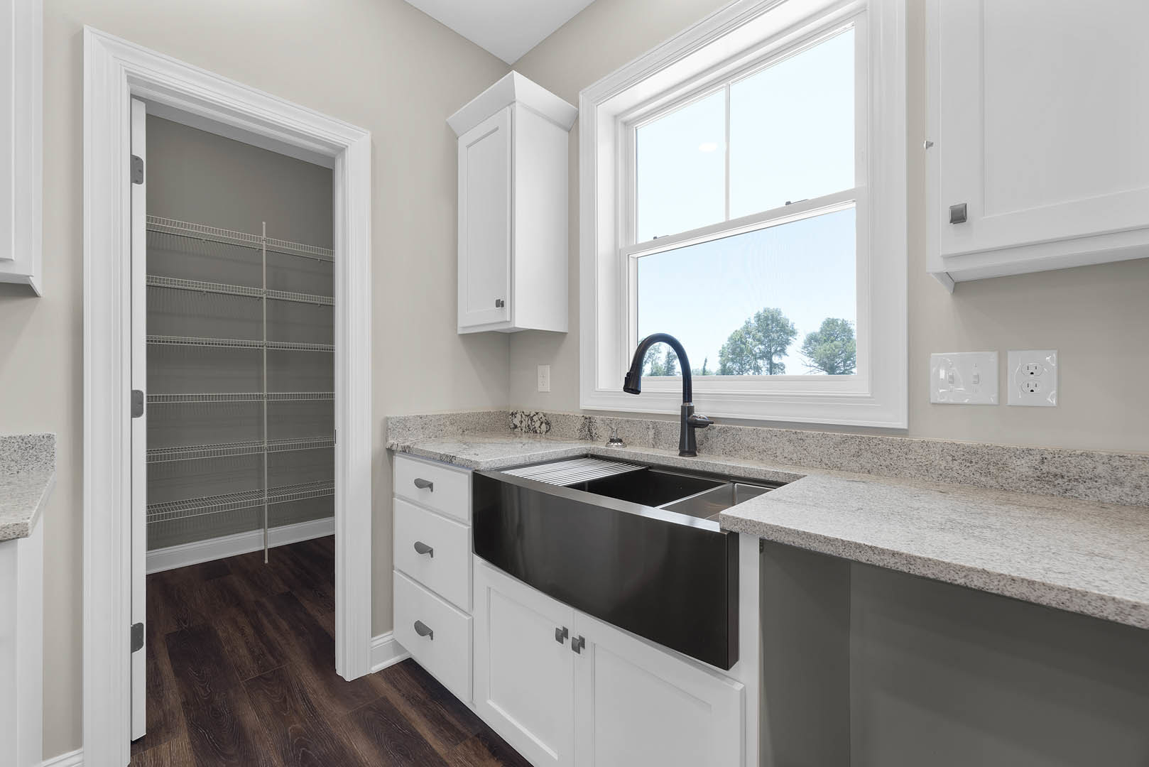 White cabinetry and tile backsplash in a kitchen with stainless steel sink, black faucet, and large window overlooking trees