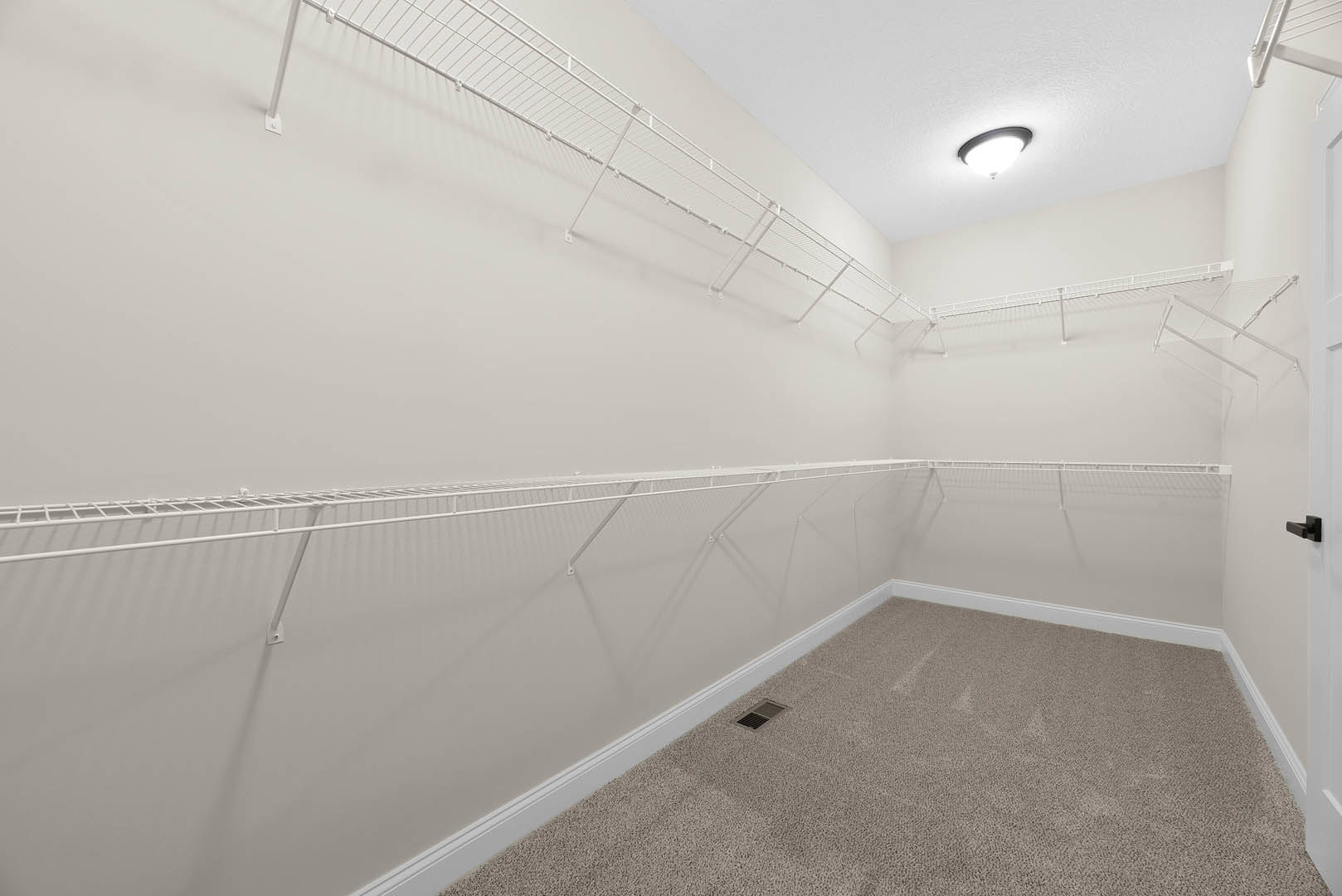 White built-in shelves along a wall, beige carpet flooring, white ceiling with recessed light fixture and air vent, white metal railing visible in foreground.