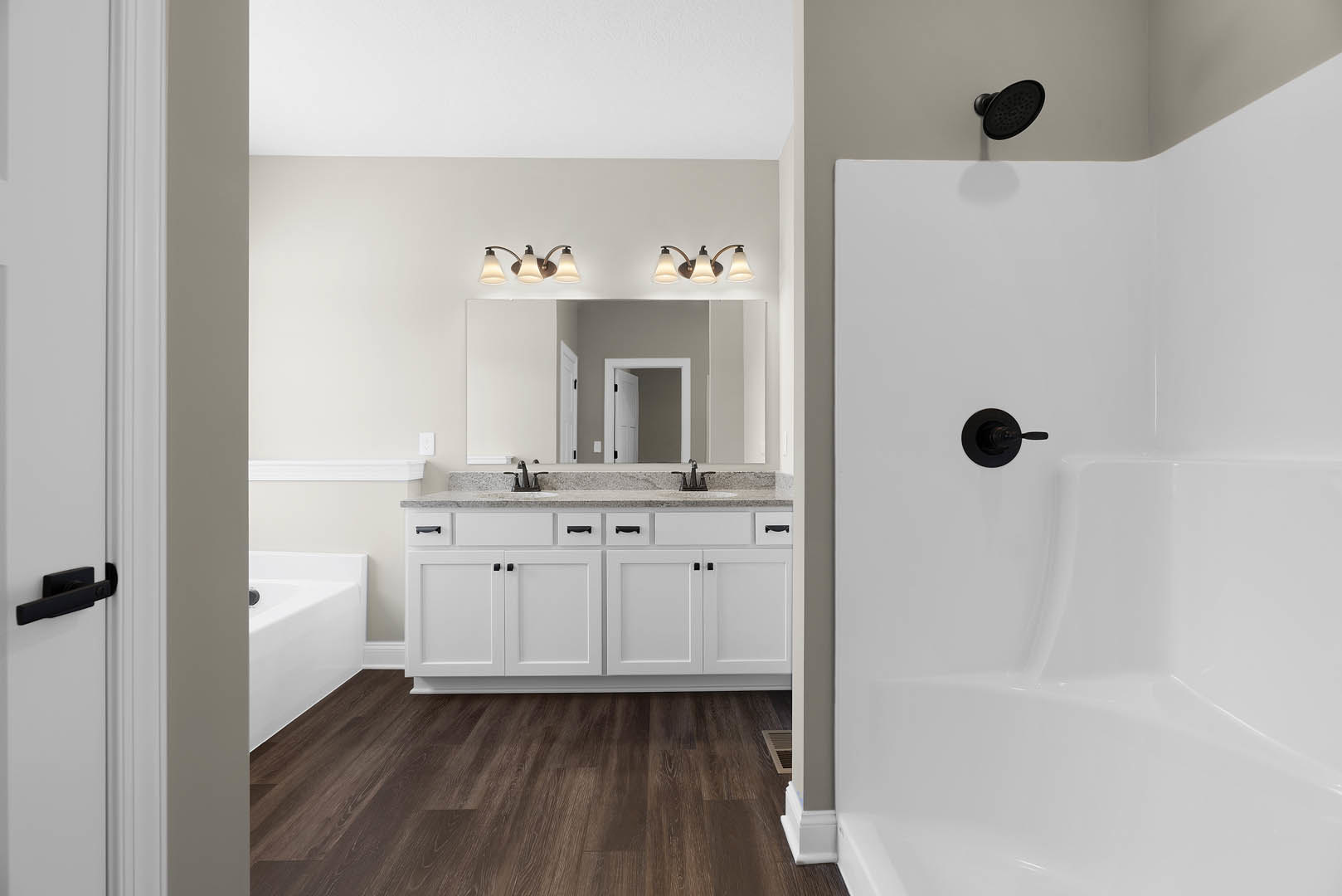 Bathroom with white freestanding bathtub, white shaker cabinets with black handles, glass shower enclosure featuring black round shower head and black handle, white door with