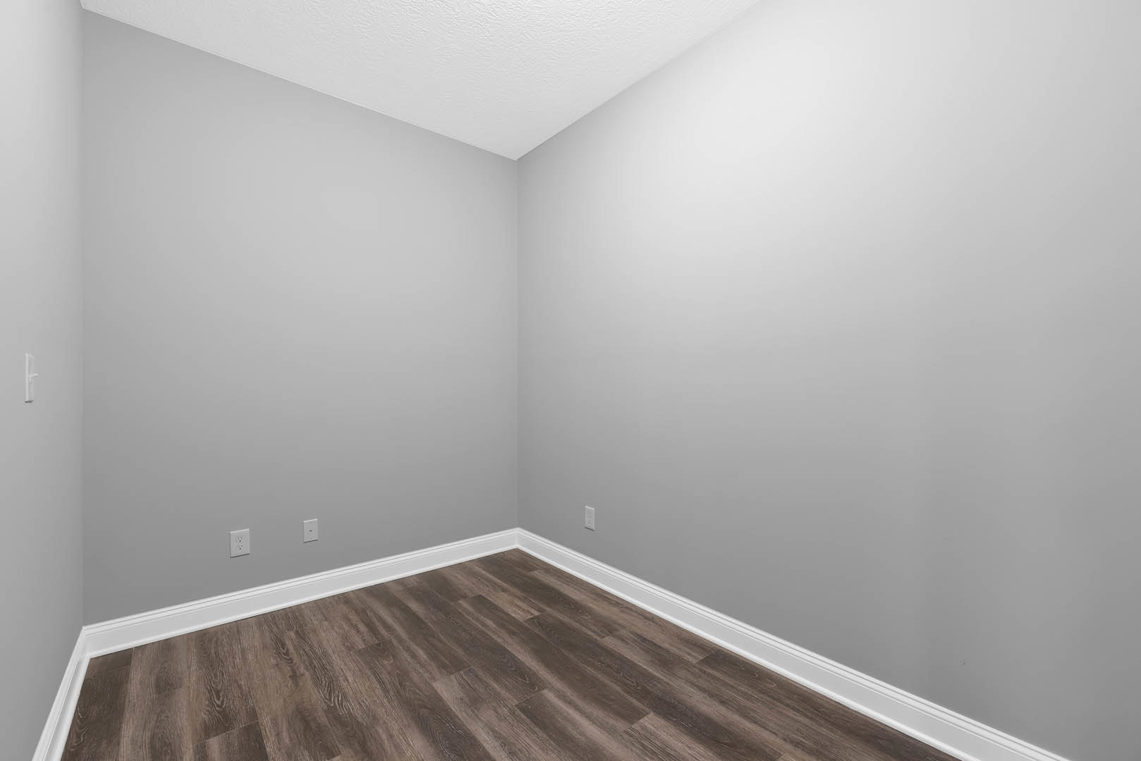 Wood flooring with white baseboards, white walls, and a white ceiling featuring a central light fixture