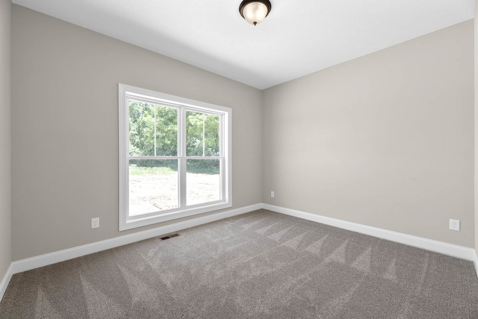 Neutral-toned carpeted room with white walls, large window overlooking trees, ceiling fan with light fixture, and crown molding accents