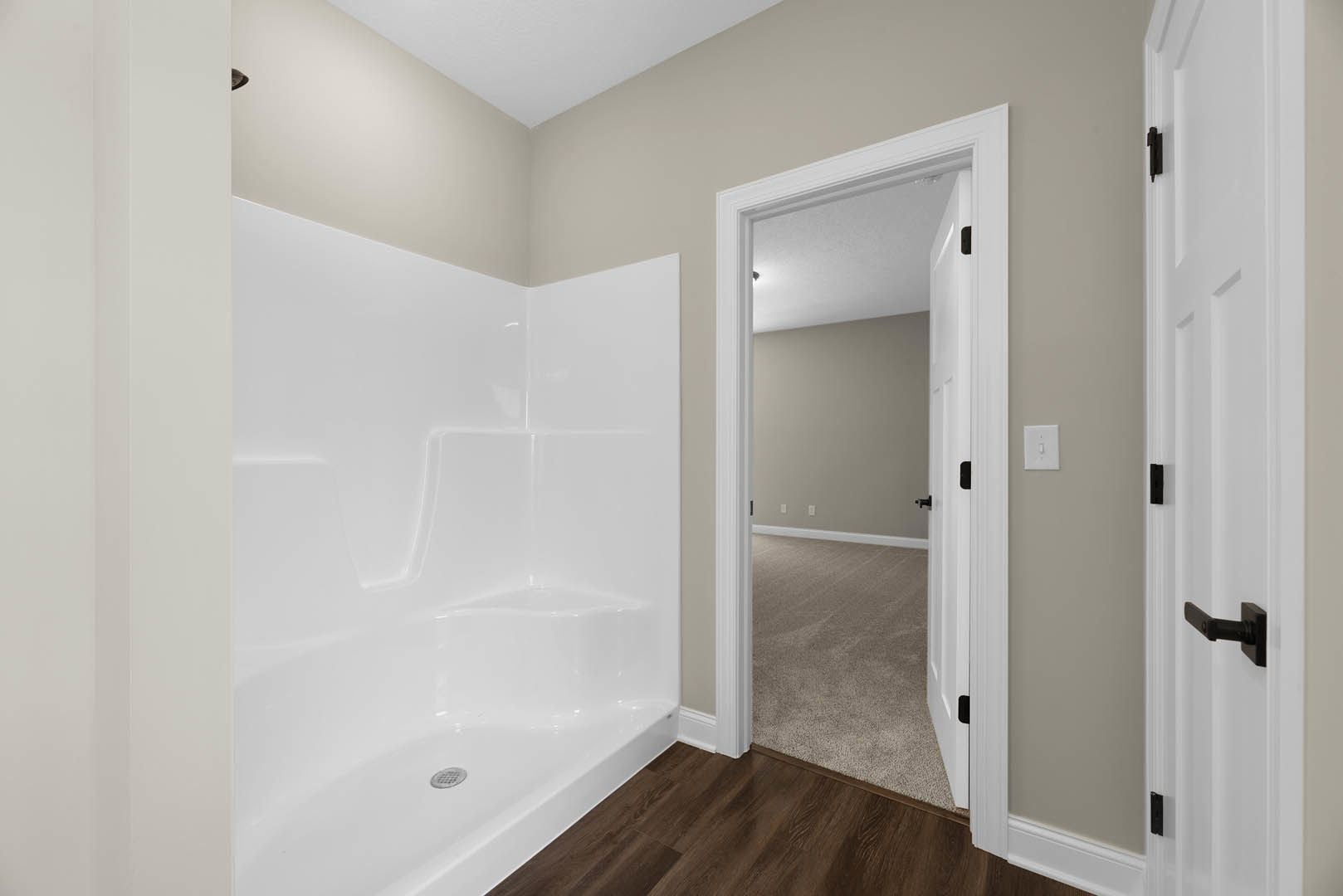 Bathroom with white tub and metal frame, wood flooring, open door revealing carpeted adjacent room, light switch on plaster wall, white molding along ceiling.
